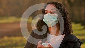 Mixed race African American girl biracial teenager young woman wearing a face mask drinking takeout coffee