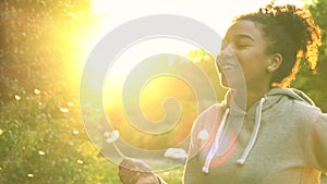 Mixed race African American girl teenager girl young woman blowing dandelion at sunset