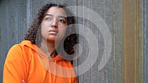 Mixed race African American girl teenager young woman looking sad wearing an orange hoodie in an urban city environment