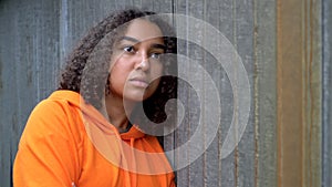 Mixed race African American girl teenager young woman looking sad wearing an orange hoodie in an urban city environment