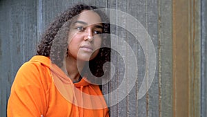 Mixed race African American girl teenager young woman looking sad wearing an orange hoodie in an urban city environment