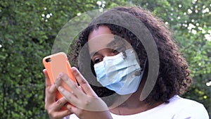 Mixed race African American girl teenager young woman wearing a face mask during COVID-19 Coronavirus pandemic using her smartphon
