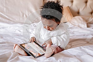 Mixed race African black toddler baby girl watching cartoons on tablet. Ethnic diversity. Little kid child using technology. Early