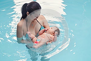 Mixed race asian mother training teaching her newborn baby to float in swimming pool