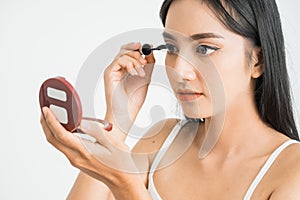 mixed race asian woman putting mascara on eyelashes on white background