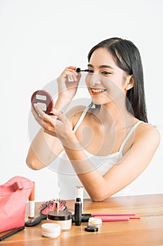 mixed race asian woman putting mascara on eyelashes on white background