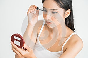 mixed race asian woman putting mascara on eyelashes on white background