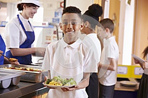 Mixed race boy holding a plate of food in a school cafeteria photo