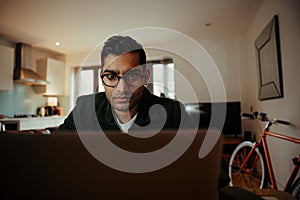 Mixed race businessman concentrating while working off digital laptop sitting at home office