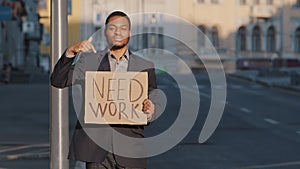 Mixed Race businessman holding sign Need Work points index finger. Portrait of Young man standing outdoor hold poster