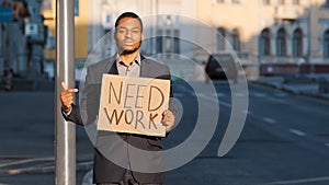 Mixed Race businessman holding sign Need Work points index finger. Portrait of Young man standing outdoor hold poster