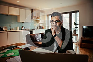 Mixed race businessman seated concentrating while working on laptop sitting at home office