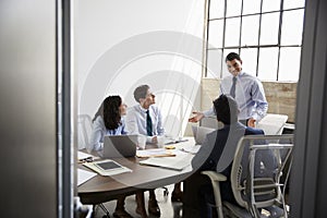 Mixed race businessman stands addressing team in a meeting