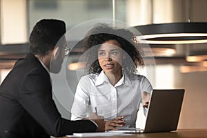 Mixed race businesswoman and colleague discussing project, using laptop