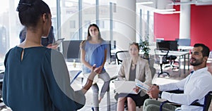 Mixed race businesswoman holding file and talking to diverse colleagues at casual office meeting