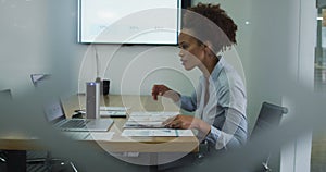 Mixed race businesswoman sitting at desk, checking documents and using laptop in office