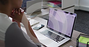 Mixed race businesswoman sitting at desk and using laptop with copy space on screen in office