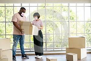 Mixed Race couple American African and Asian a surgical mask is carrying cardboard boxes in a new house on moving day. Concept of