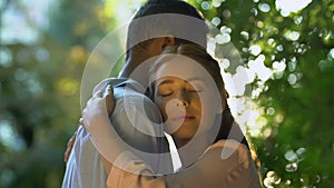 Mixed-race couple embracing lovingly, enjoying romantic feelings in sunny forest