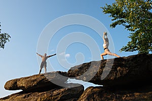 Mixed race couple of fitness trainers doing exercises on the rocky peak. Sport and health care concept.