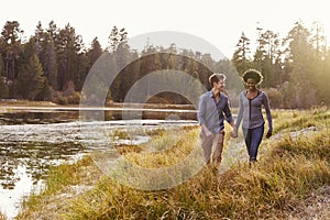 Mixed race couple holding hands, walking near a rural lake