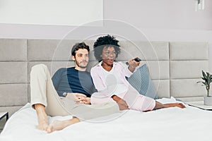 Mixed race couple resting on bed and watching TV together in day-off
