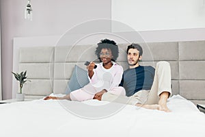 Mixed race couple resting on bed and watching TV together in day-off