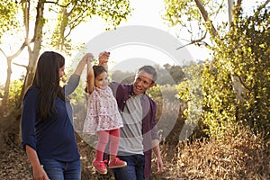 Mixed race couple walk on rural path lifting young daughter