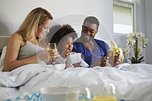 Mixed race couple and young daughter eating in bed together