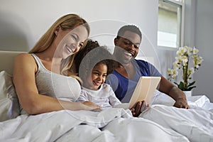 Mixed race couple and young daughter laugh in bed together