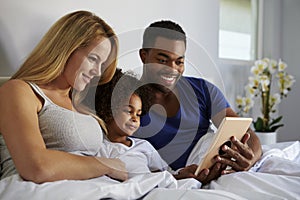 Mixed race couple and young daughter relax in bed together