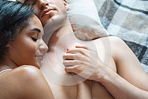 Mixed Race Couple. Young man and woman lying on bed on blanket top view sleeping holding hands smiling peaceful close-up