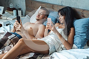 Mixed Race Couple. Young woman looking curious at man`s smartphone at home lying on bed browsing internet