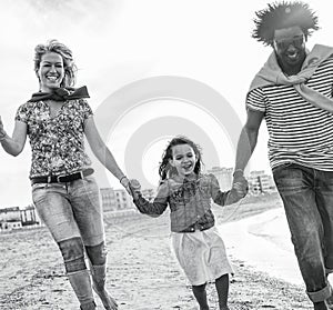 Mixed race family friends running on the beach - Diverse culture parents and child playing together - New multi ethnic families