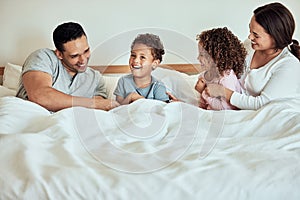 Mixed race family lying in bed, smiling and playing. Latino parents having fun with their little cute kids. Brother and