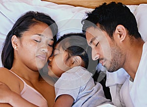 Mixed race family, mother, father and daughter resting on the white bed in the bedroom at home. Tired parents lying in