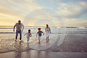 Mixed race family running in the water and having fun together on the beach. Parents spending time with their daughter