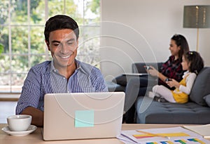 Mixed race family sharing time in living room. Caucasian father using notebook computer to work, half-Thai girl and Asian mother