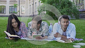 Mixed-race fellows having rest on lawn on college campus, enjoying hobbies