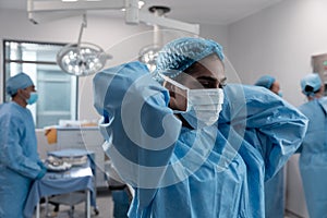 Mixed race female doctor putting on face mask standing in operating theatre