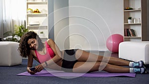 Mixed race female lying on floor in sportswear, using phone, procrastination