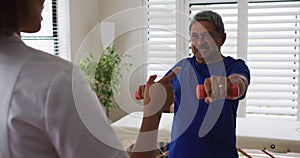 Mixed race female physiotherapist helping senior man exercise using dumbbells