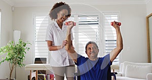 Mixed race female physiotherapist helping senior man exercise using dumbbells