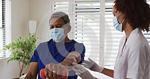 Mixed race female physiotherapist wearing mask helping senior exercise using dumbbells