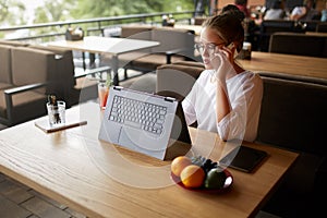 Mixed race freelancer working with convertible laptop and talking on cellphone with client in cafe. Asian caucasian