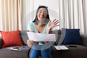 Mixed race gender fluid man working at home making video call holding documents, smiling and waving photo