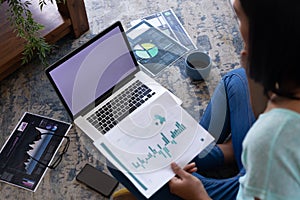Mixed race gender fluid man working at home sitting on floor using laptop, copy space screen photo