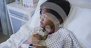 Mixed race girl lying on hospital bed wearing fingertip pulse oximeter and holding teddy bear