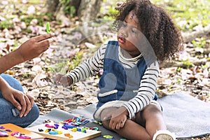mixed race girl sitting on lawn with leaves and looking at plasticine on hands mother in the park.