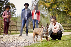 Mixed race girl squatting to pet her dog during a family walk in the countryside looking to camera, low angle